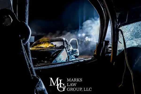A wrecked car at night seen through the shattered window of another vehicle