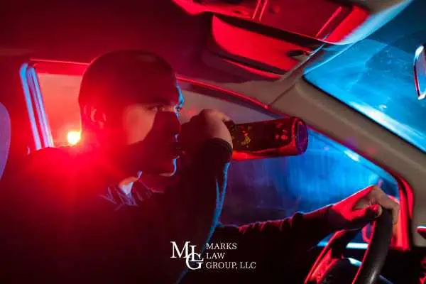 Man drinking from a bottle behind the wheel under red and blue police lights
