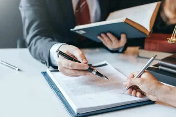 two people in suits signing a document with pens at a desk