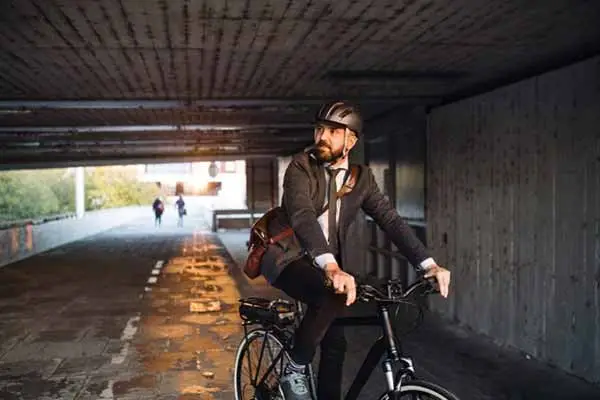 bearded man in a helmet and coat riding a bicycle through a concrete underpass