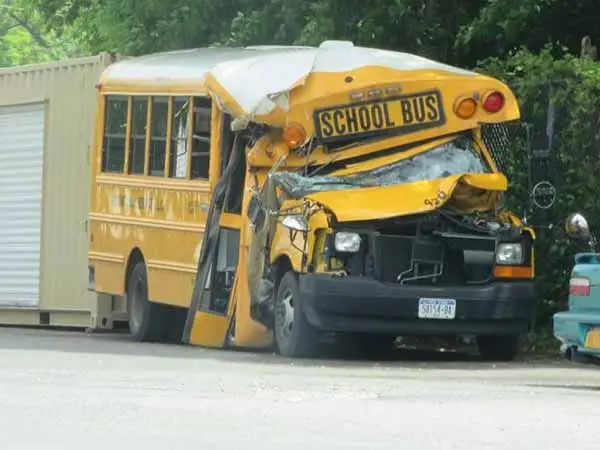 yellow school bus with a crushed front end parked beside a storage container
