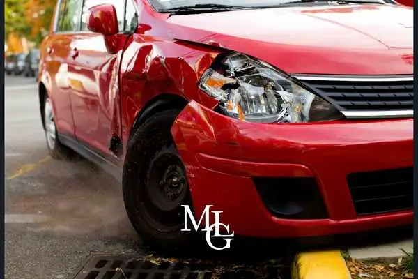 Front corner of a red hatchback with a dented wing and smashed headlight