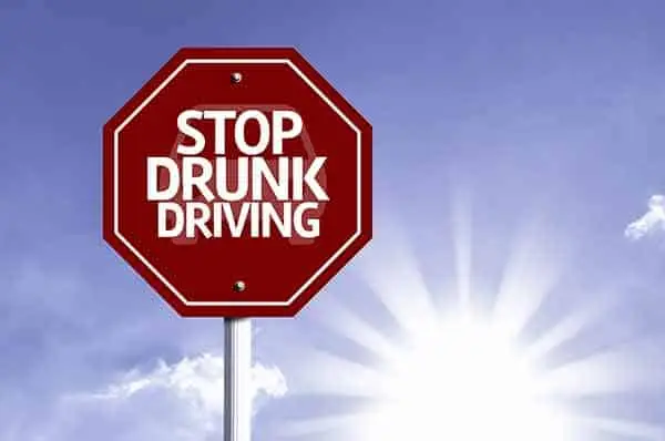red octagonal road sign reading "stop drunk driving" against a sunlit blue sky