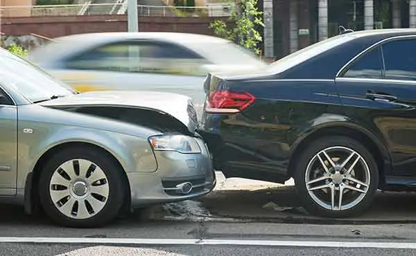 silver car rear-ends a black sedan on a city street