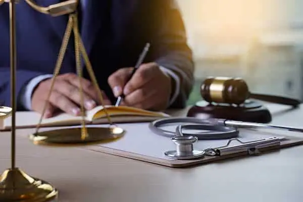 man in a suit writing at a desk with gavel, stethoscope and brass scales