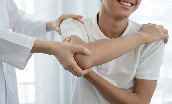 clinician in a white coat examining a smiling man's elbow and shoulder