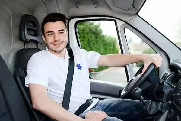 smiling man in a white polo at the wheel of a van, seatbelt fastened
