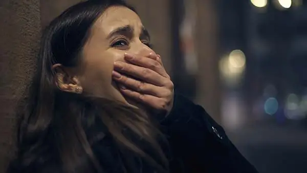 distressed young woman covering her mouth against a wall at night