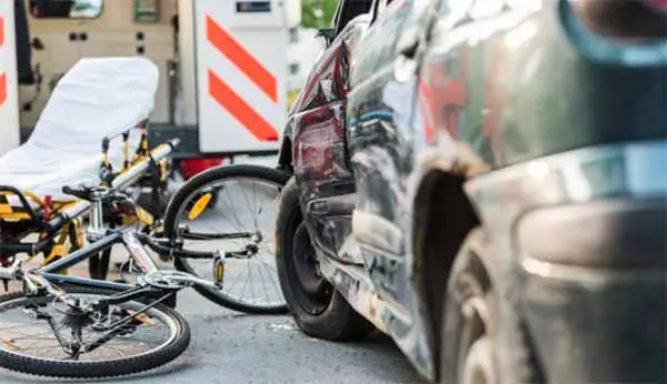 A bicycle lying against a damaged car with an ambulance stretcher nearby