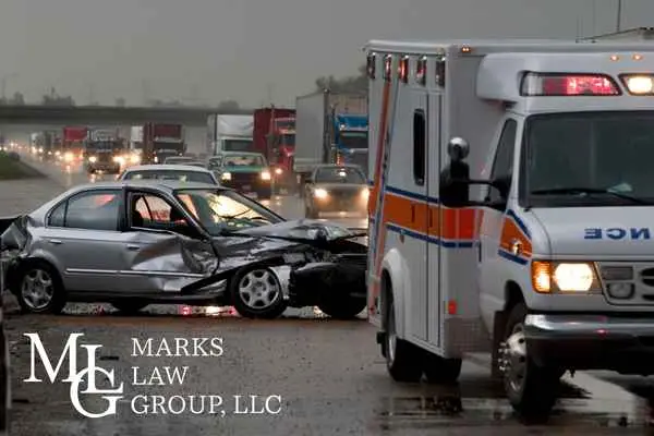 An ambulance pulling up to a wrecked car on a wet highway