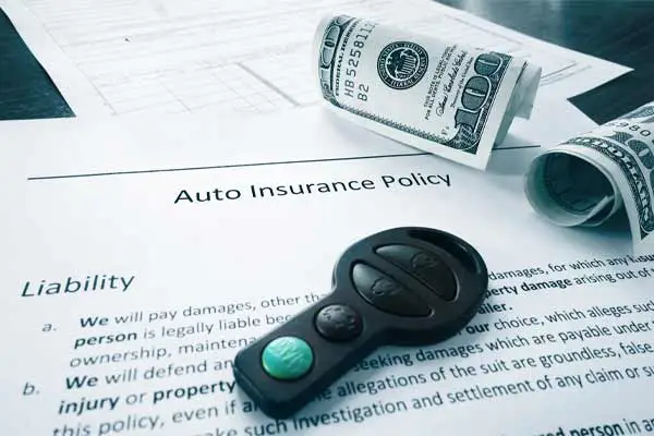An auto insurance policy page with a car key fob and rolled hundred dollar bills