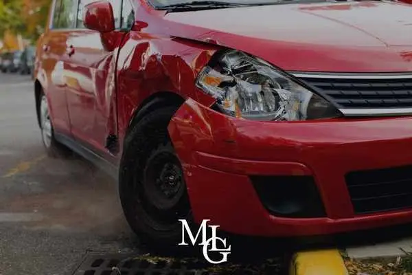 Front corner of a red hatchback with a dented wing and smashed headlight
