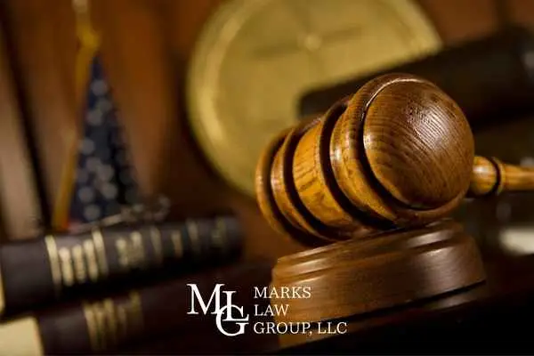 A wooden gavel on a desk with law books and a folded flag behind it