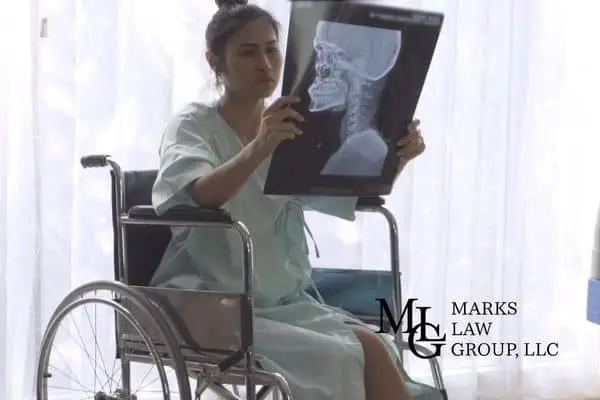 Woman in a hospital gown in a wheelchair examining a neck and skull x-ray