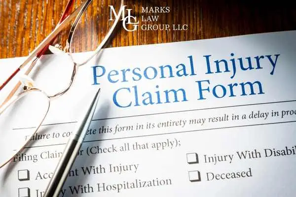 A personal injury claim form with tick boxes, reading glasses and a pen on a desk