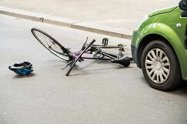 A bicycle and a helmet lying on the road beside a green car