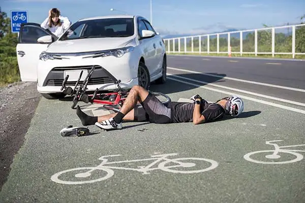 A cyclist lying in a bike lane beside a fallen bicycle and a stopped white car