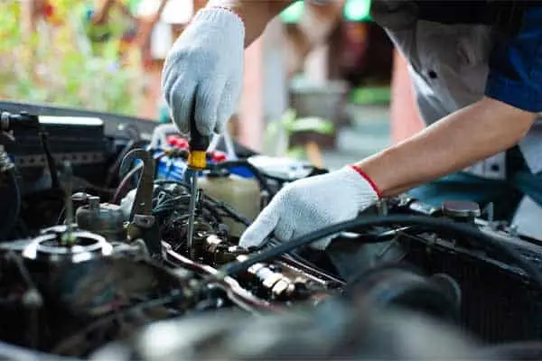 Mechanic in work gloves repairing an engine under an open car hood