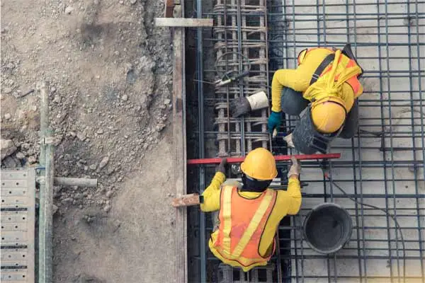 overhead view of two workers in hard hats tying rebar in a concrete form