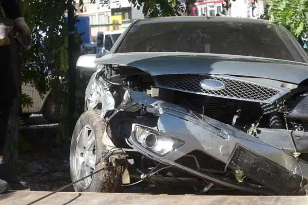 silver car with crushed front end and torn-off bumper hanging down