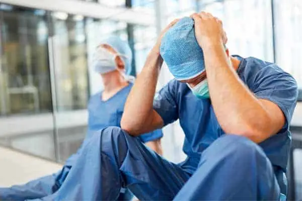 man in blue scrubs and mask sitting on floor holding his head