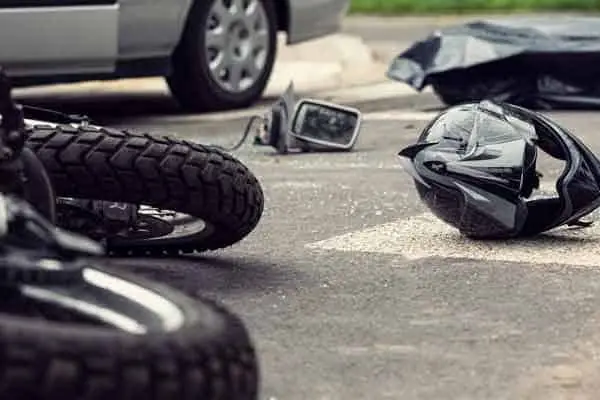 motorcycle lying on the road with a helmet and broken mirror nearby