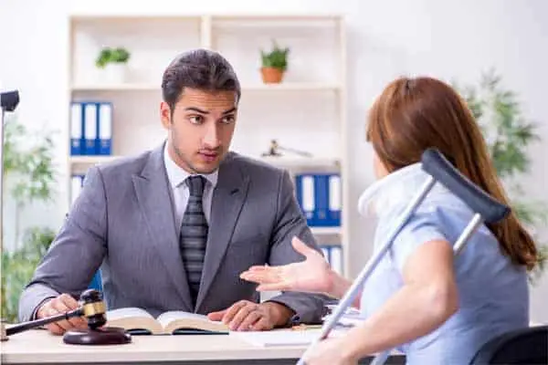 man in a suit at a desk talking with a woman in a neck brace