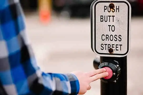 hand pressing a crossing button under a sign reading "push butt to cross street"