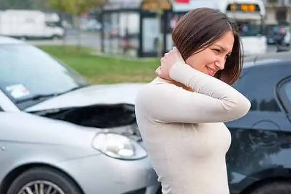 woman holding her neck in pain in front of two crashed cars