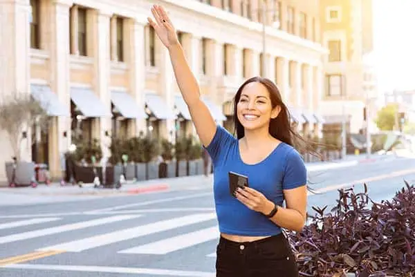 smiling woman raising her hand to hail a ride on a city street