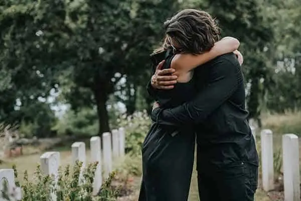 two people in black embracing among white headstones in a cemetery