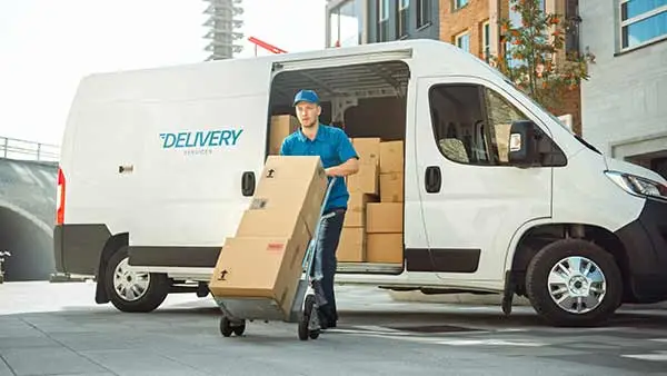 Courier wheeling stacked boxes out of a white delivery van
