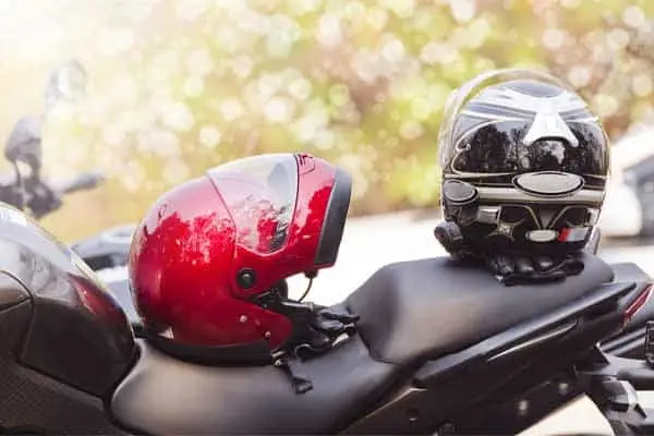 A red and a black motorcycle helmet resting on a parked motorcycle