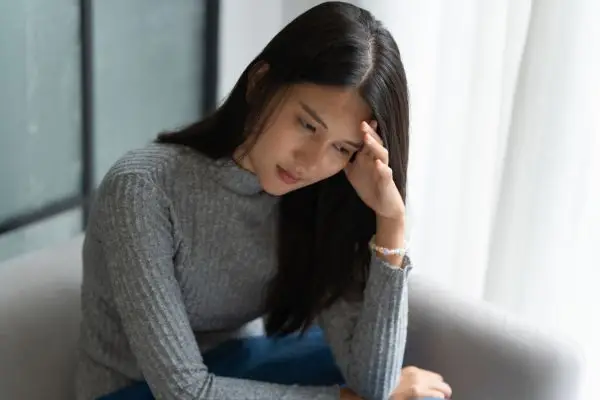 Woman sitting on a couch, holding her head and looking stressed or worried.