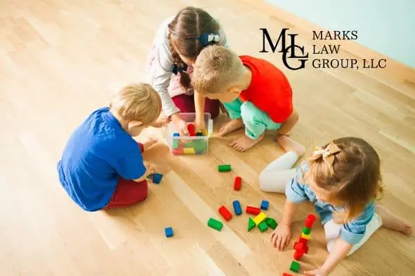 Four young children on a wooden floor playing with coloured building blocks