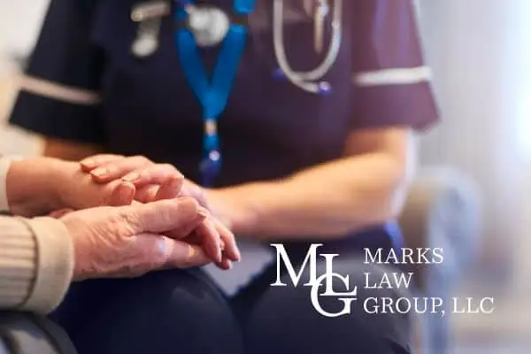 A nurse in uniform holding the hands of an elderly seated patient
