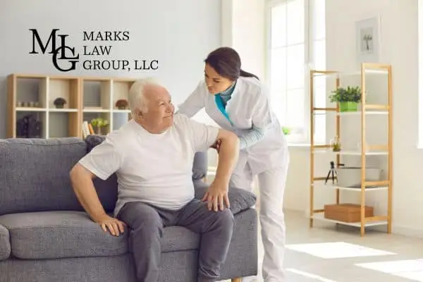 A nurse helping an elderly man rise from a sofa in a bright room