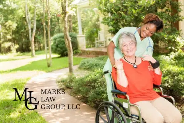 Nurse pushing a smiling elderly woman in a wheelchair along a garden path
