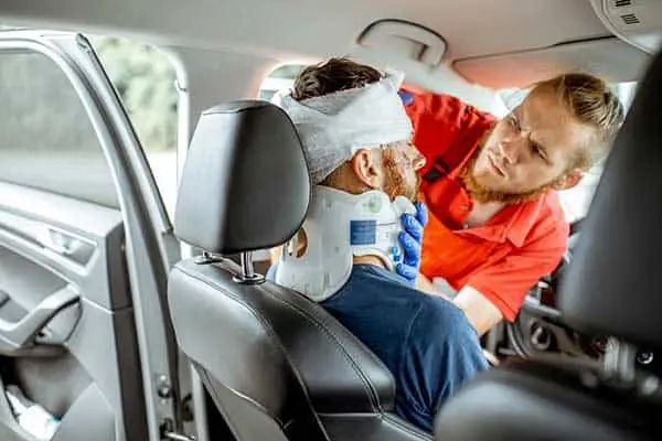 A paramedic bandaging the head of an injured man still sitting in a car