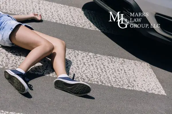 A person lying on a crosswalk in front of a stopped car's bumper