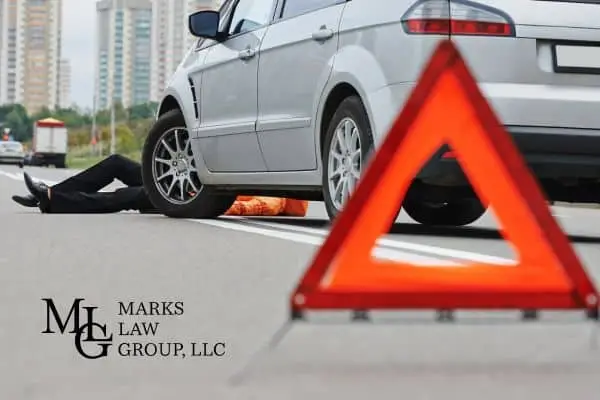 A person lying in the road beside a car with a red warning triangle in front