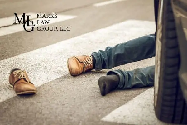 Legs of a person lying in a crosswalk beside a car tyre, one shoe thrown clear
