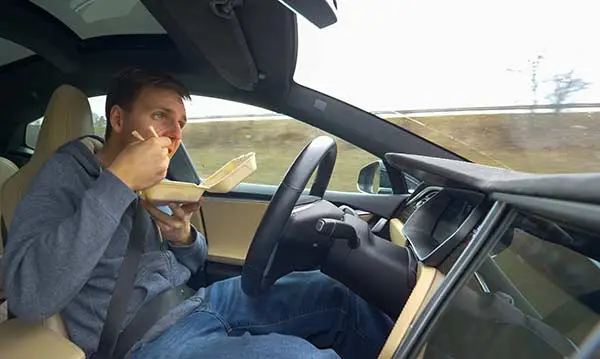 A driver eating from a container with both hands off the steering wheel