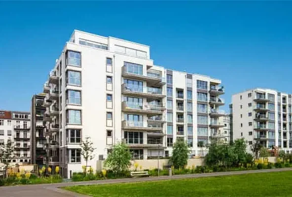 Modern white apartment blocks with balconies behind a green lawn