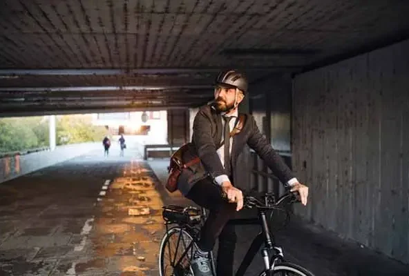 Man in a suit and helmet riding a bicycle through a dim underpass