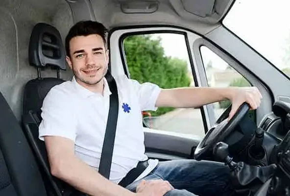 Smiling driver in a white polo at the wheel of a medical transport van