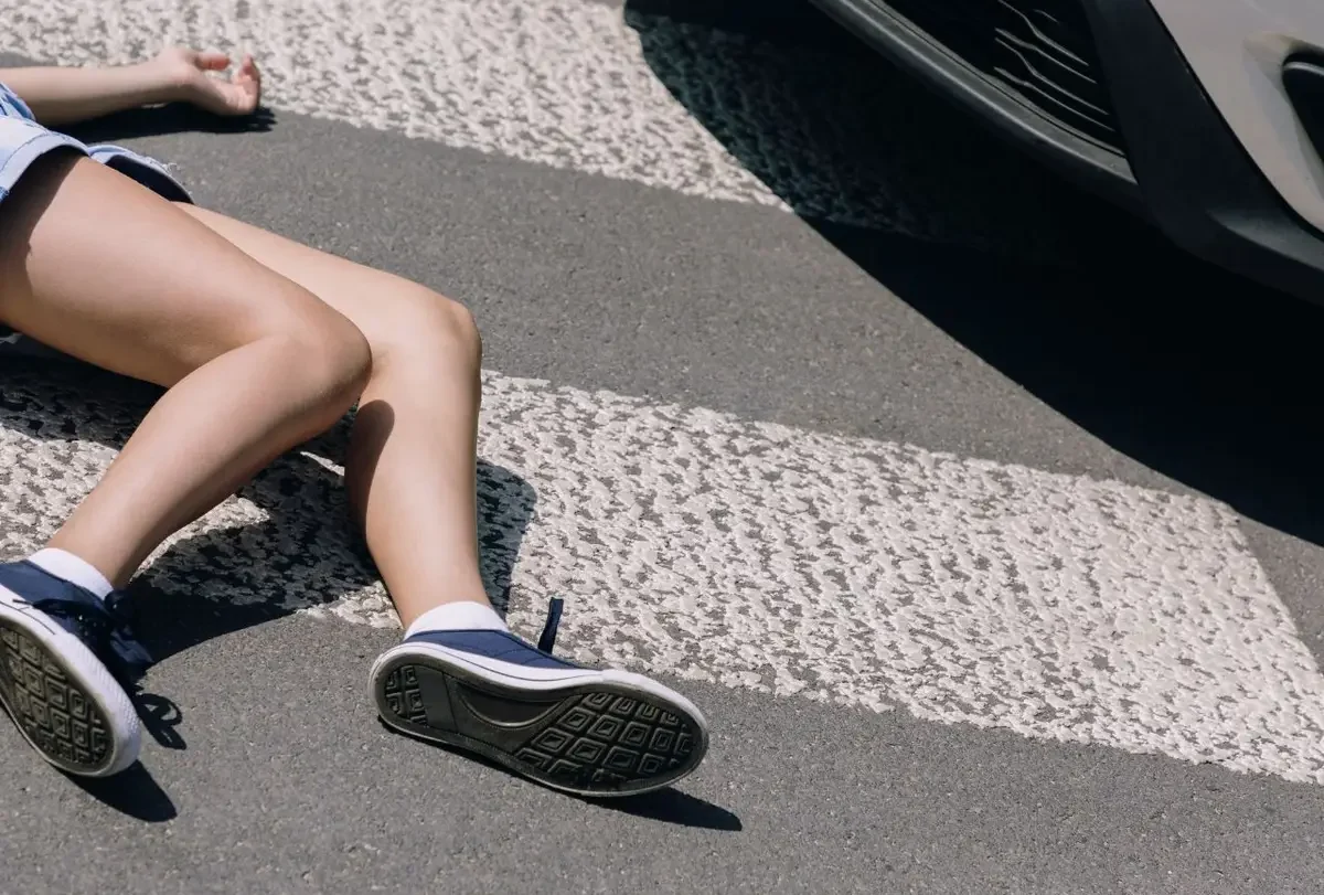 Person lying on a crosswalk beside the front bumper of a car