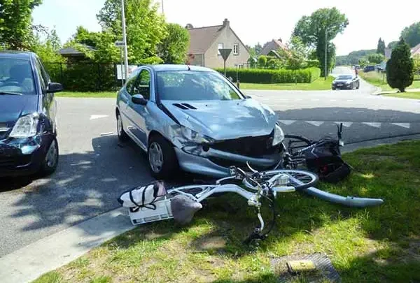 Silver car with a crushed front end and a wrecked bicycle on the grass