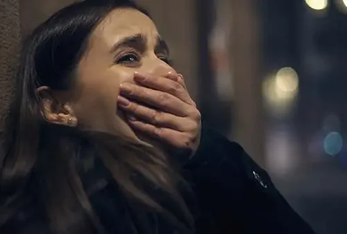 Distressed woman covering her mouth against a wall at night