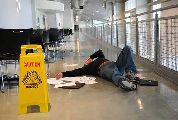 Man lying on a lobby floor beside a yellow caution wet floor sign